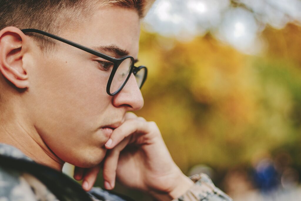 Photo of a young teen or adult male profile face who appears to be reading or thinking. Hes wearing glasses, and has his chin resting on one hand.