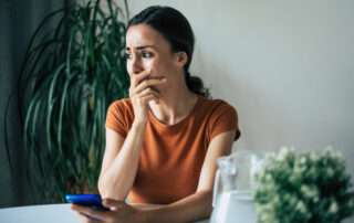 Sad, frustrated young brunette woman is crying with smartphone in hands