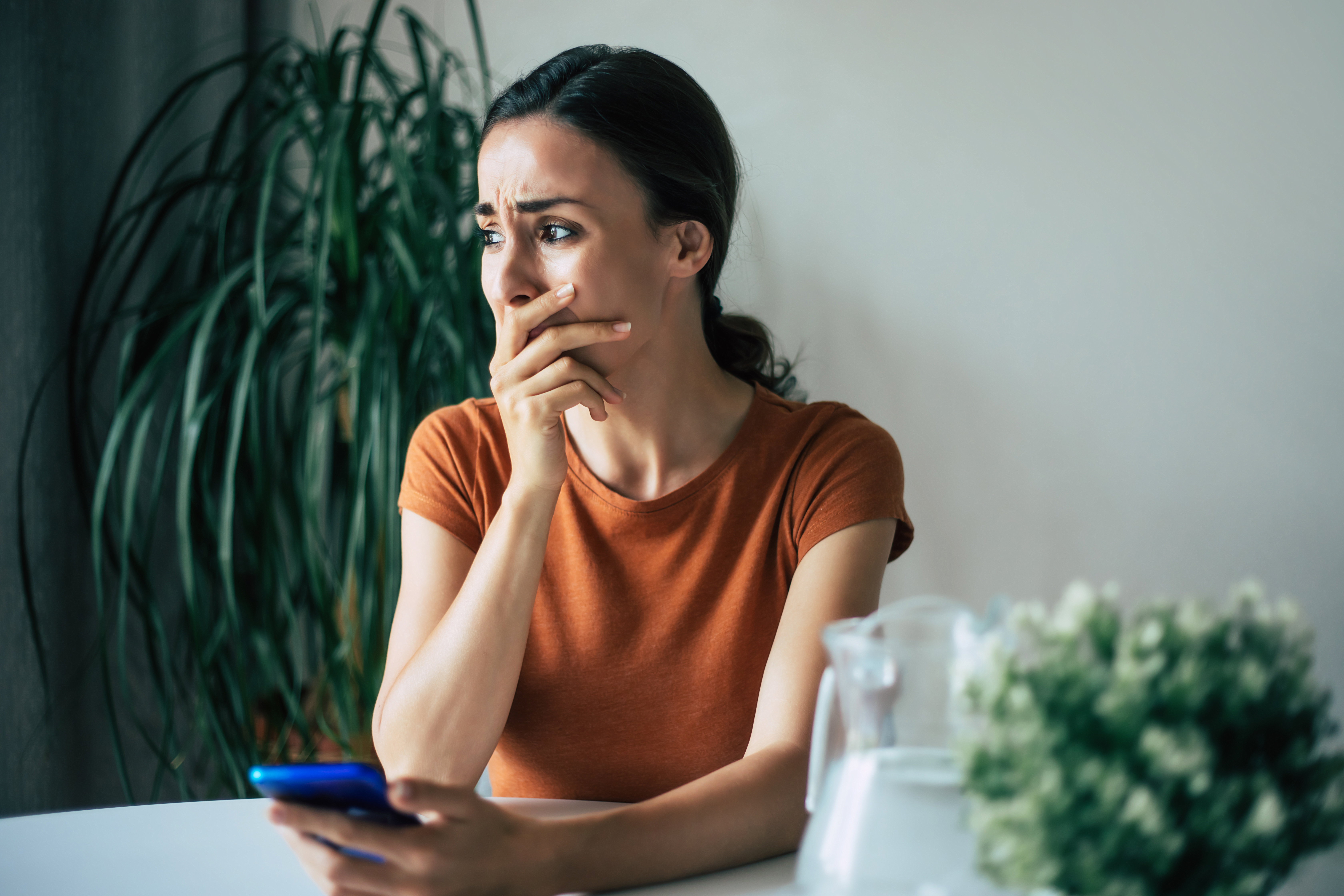 Sad, frustrated young brunette woman is crying with smartphone in hands