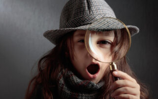 The surprised little detective with a magnifying glass. A little girl in a hat and coat is playing detective. Copy space.